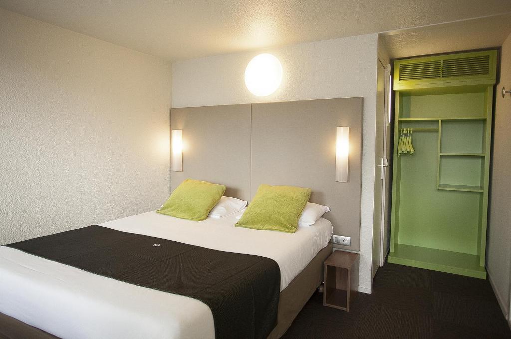 a bedroom with a large bed with two green pillows at Campanile Nîmes Sud - Caissargues in Caissargues
