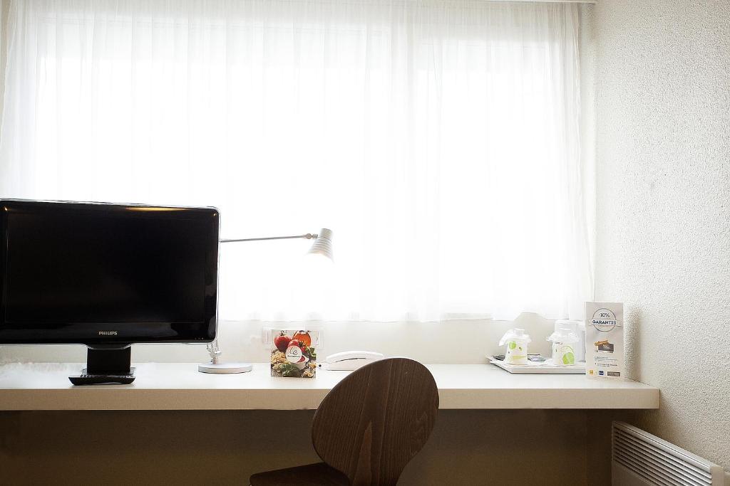 a television sitting on a desk in front of a window at Campanile Nîmes Sud - Caissargues in Caissargues