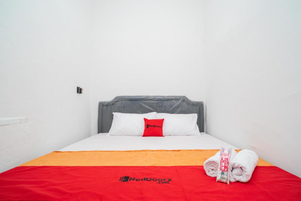 a bed with a red pillow and a red blanket at RedDoorz @ Aralia Harapan Indah in Pulokendal