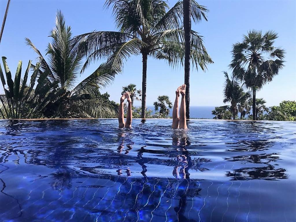 Una piscina con dos personas en el agua con palmeras en Villa Cantik Sambirenteng en Gretek