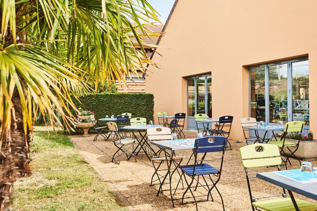 un patio con mesas, sillas y una palmera en Kyriad Direct Lyon Sud - Chasse-Sur-Rhône en Chasse-sur-Rhône