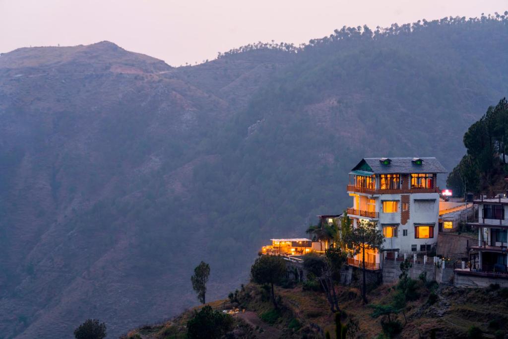 a house on a hill with mountains in the background at Zostel Banikhet (Dalhousie) in Dalhousie
