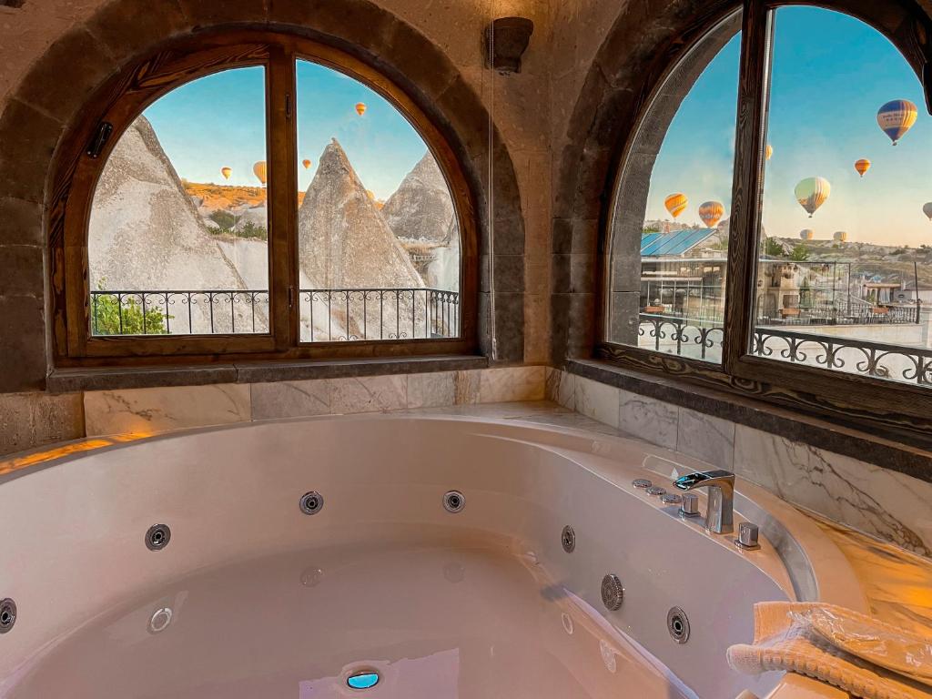 a bath tub in a room with three windows at Goreme Valley Cave House in Goreme