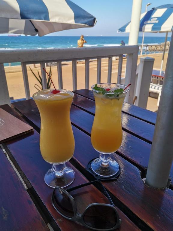 two cocktails sitting on a wooden table next to the beach at Umdloti Holiday Resort Apartments in Umdloti