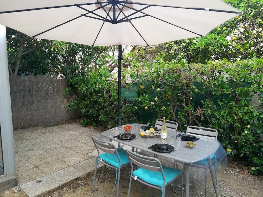 una mesa con sillas y una sombrilla en el patio en Gîte des Tamarins à Saint-Pierre la Mer en Fleury