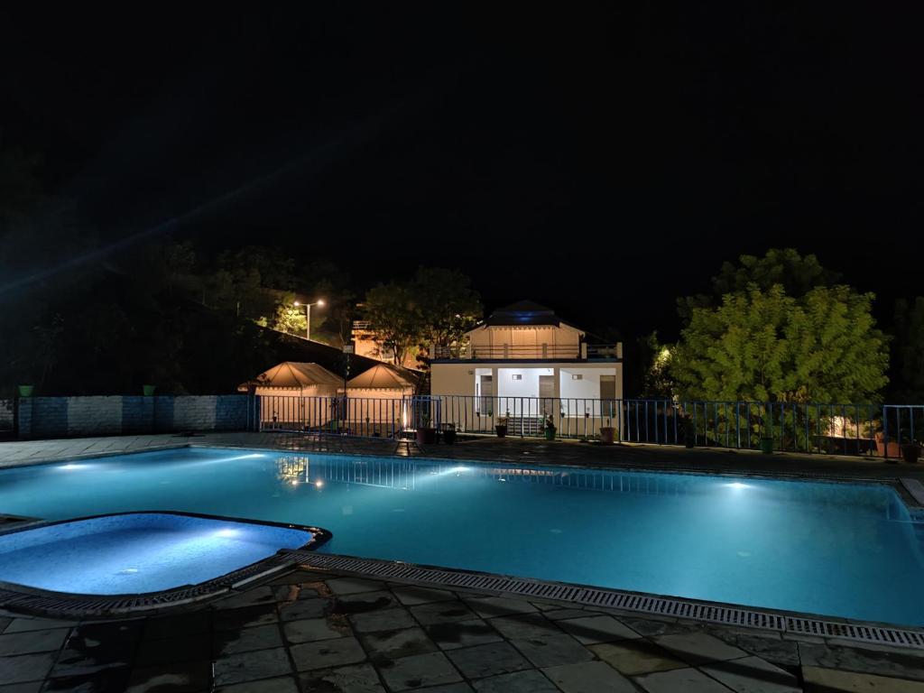 - une piscine la nuit avec une maison en arrière-plan dans l'établissement Hill View Resort by Rudrakshi, à Udaipur