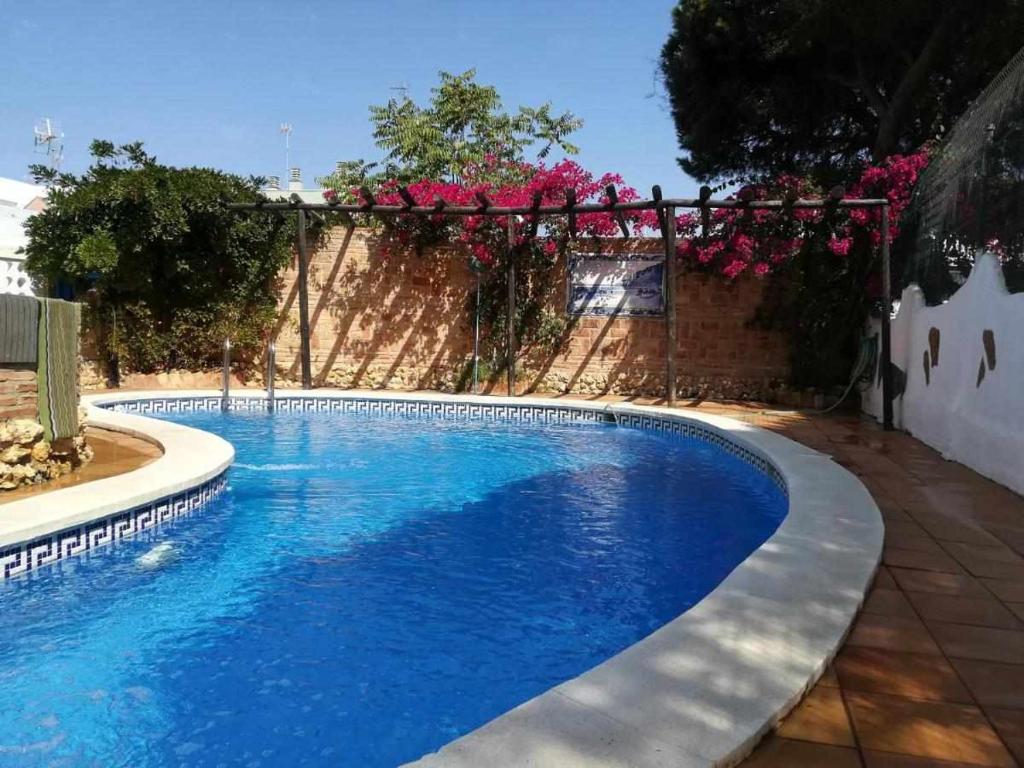 ein blauer Pool mit einem Zaun und rosa Blumen in der Unterkunft Casa Marquesa in Punta Umbría