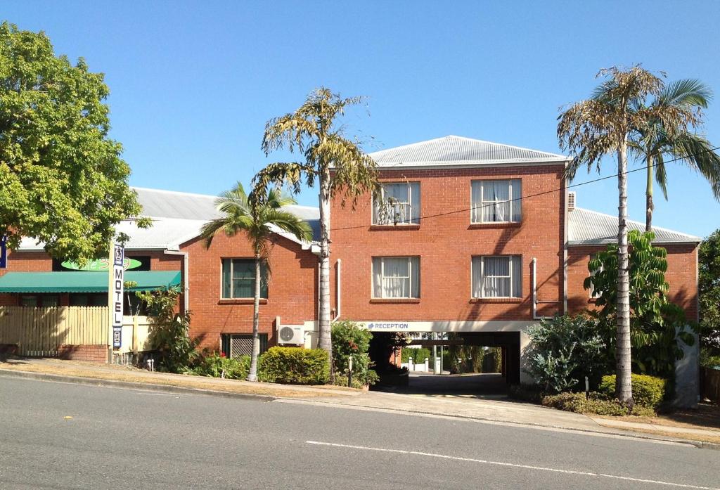 a red brick building on a street with palm trees at Greenslopes Motor Inn in Brisbane