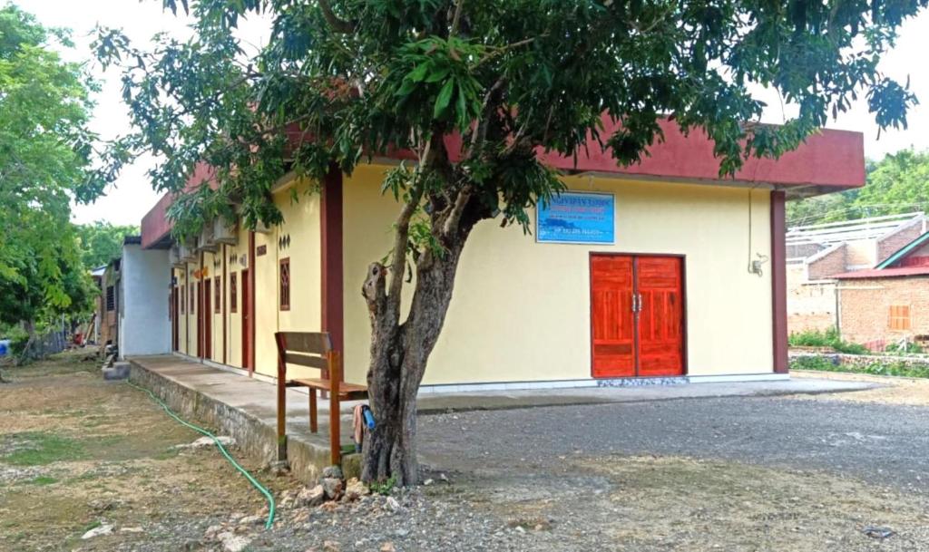 een gebouw met een rode deur en een bank naast een boom bij Penginapan asidik in Bira