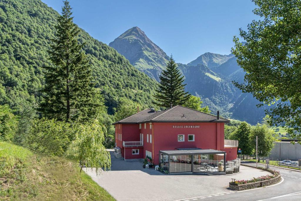 a red building with mountains in the background at Relais Lucomagno in Olivone