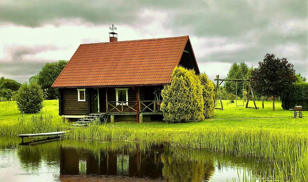 a house with a red roof sitting next to a pond at Poilsio namelis Plateliuose in Plateliai