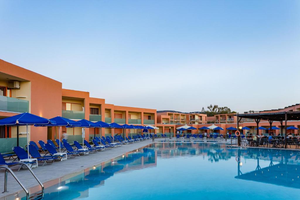 a swimming pool with blue chairs and umbrellas at Rethymno Village in Platanes