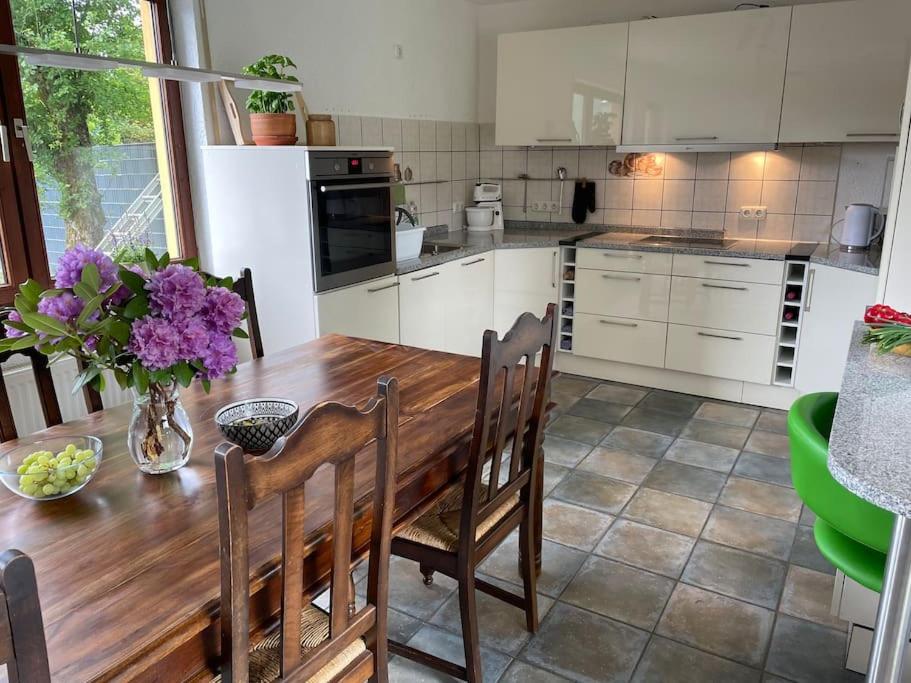 eine Küche mit einem Holztisch mit Stühlen und lila Blumen in der Unterkunft Behagliches Haus mit Kamin in Monschau