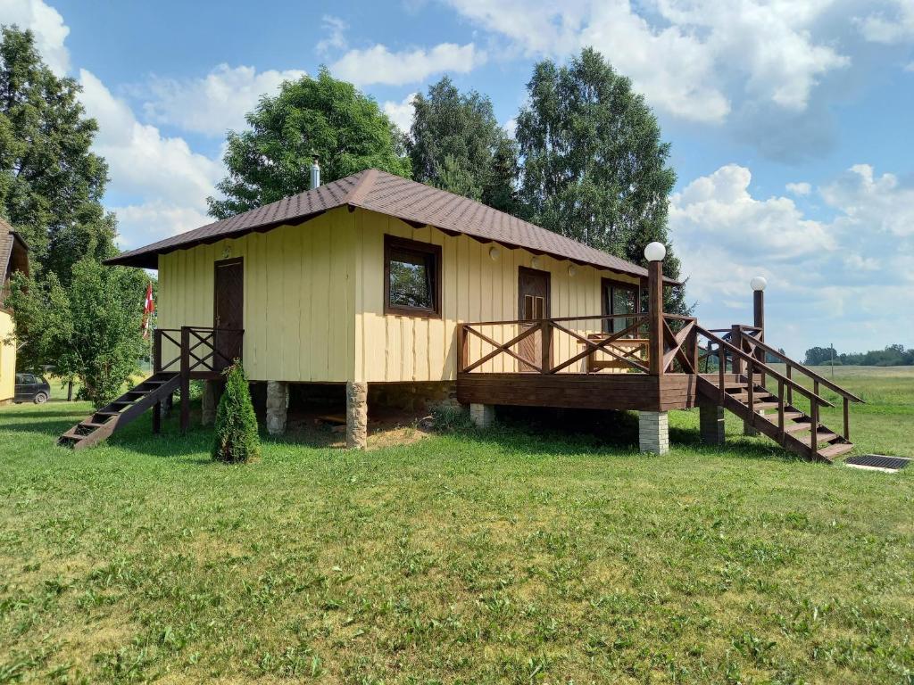 een klein geel huis met een veranda in een veld bij Rūnēnu zāļu namiņš in Vidzeme