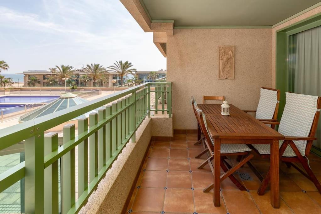 balcón con mesa de madera y sillas y piscina en ApartUP Patacona Beach I, en Valencia