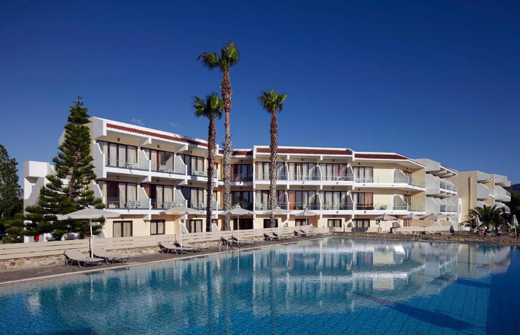 a hotel with a large swimming pool and palm trees at Atlantica Thalassa Hotel in Kos Town
