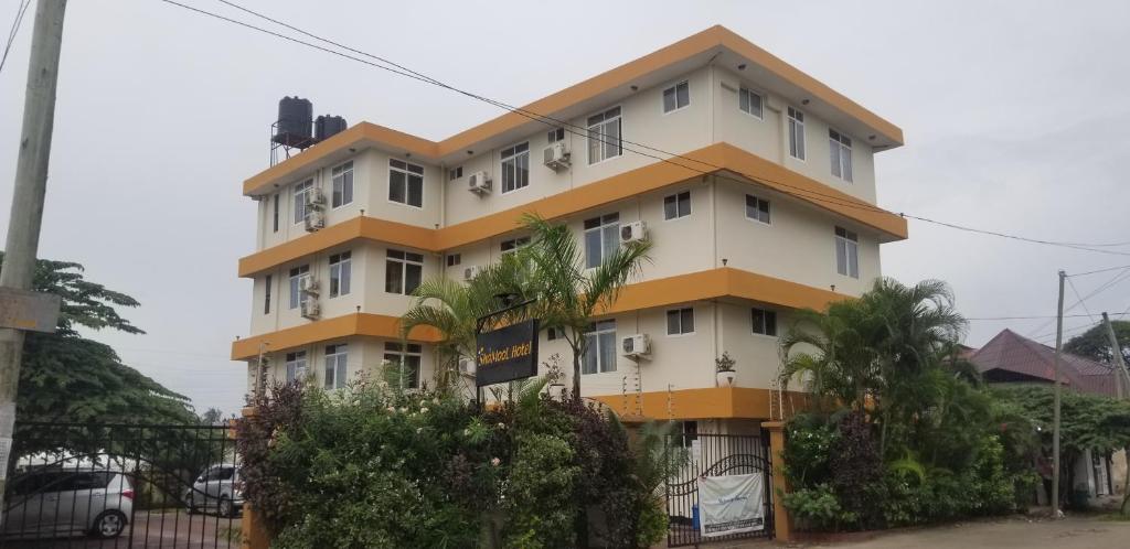 un edificio blanco y amarillo con árboles delante en ShaMooL Hotel en Dar es Salaam