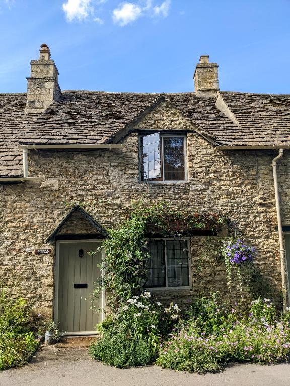 a stone house with a green door and flowers at Baker's Cottage in Castle Combe
