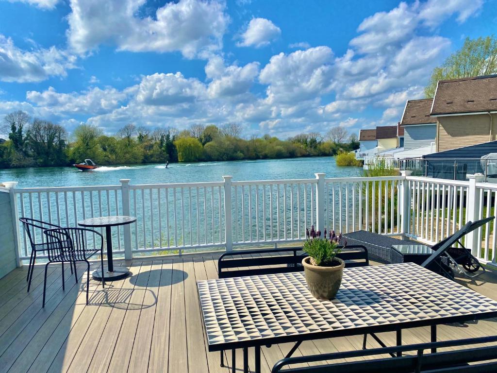 a deck with a table and chairs and a view of a river at Cotswolds Lakeside Lodge - Nesbitt's Nest in South Cerney