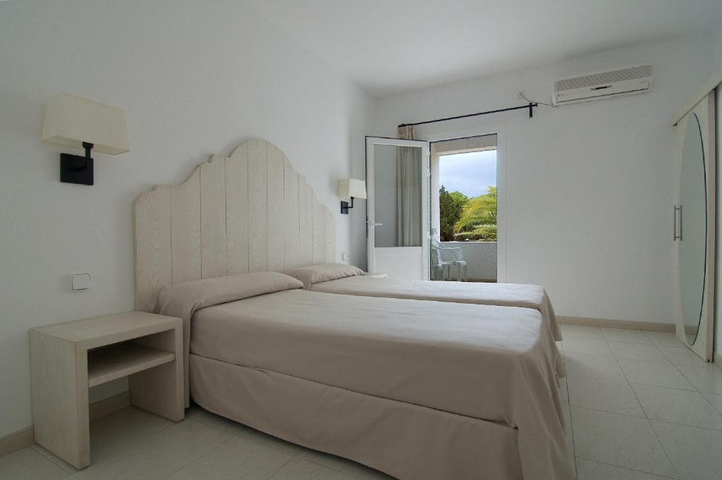 a white bedroom with a large bed and a window at Hostal Capri in Es Pujols