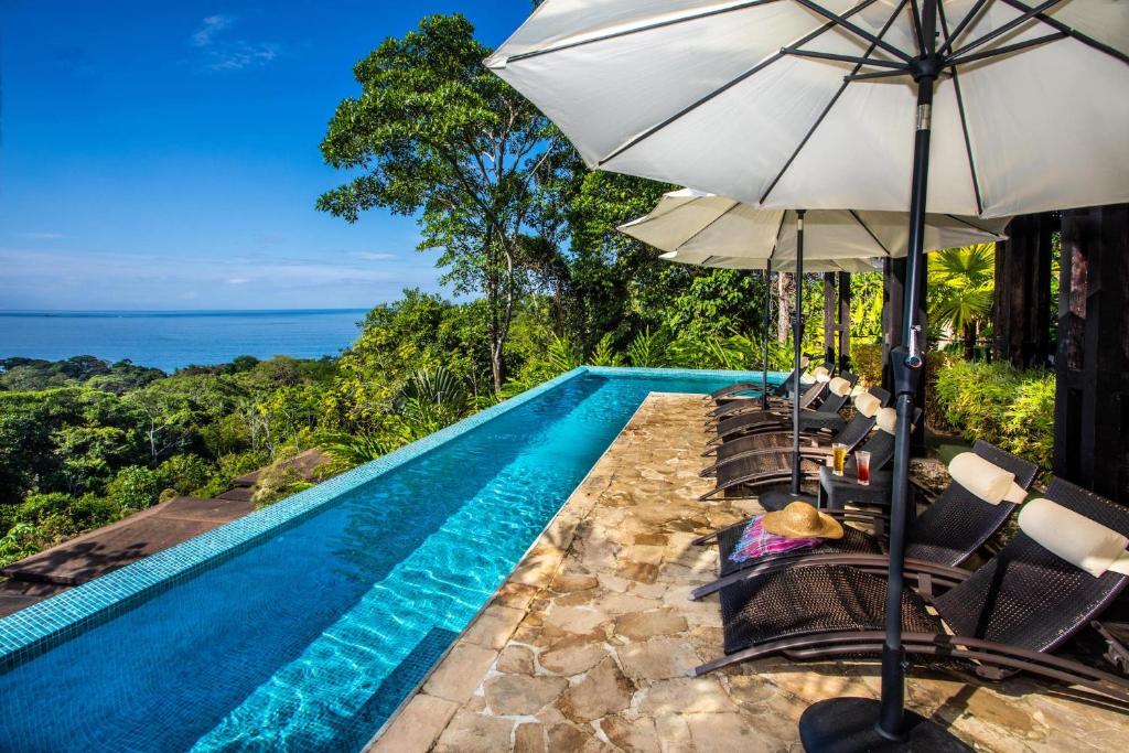a pool with chairs and an umbrella and the ocean at Tiki Villas Rainforest Lodge - Adults Only in Uvita