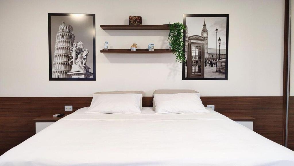 een slaapkamer met een groot wit bed met 2 foto's aan de muur bij Lindos Studios Centro/Wifi/Garagem in Foz do Iguaçu