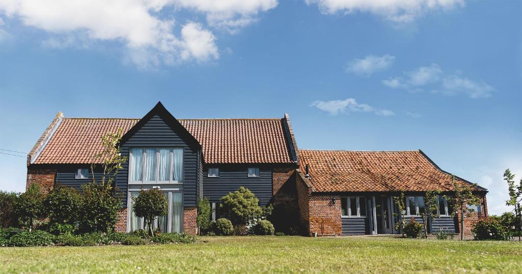 a house with a black roof on a green field at Stackyard Lodge - enchanting 18th Century converted barn in the Waveney Valley in Aldeby