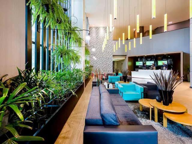 a lobby with tables and potted plants in a building at Lindo Flat Part Grand Mercure Varanda aconchegante in Brasilia