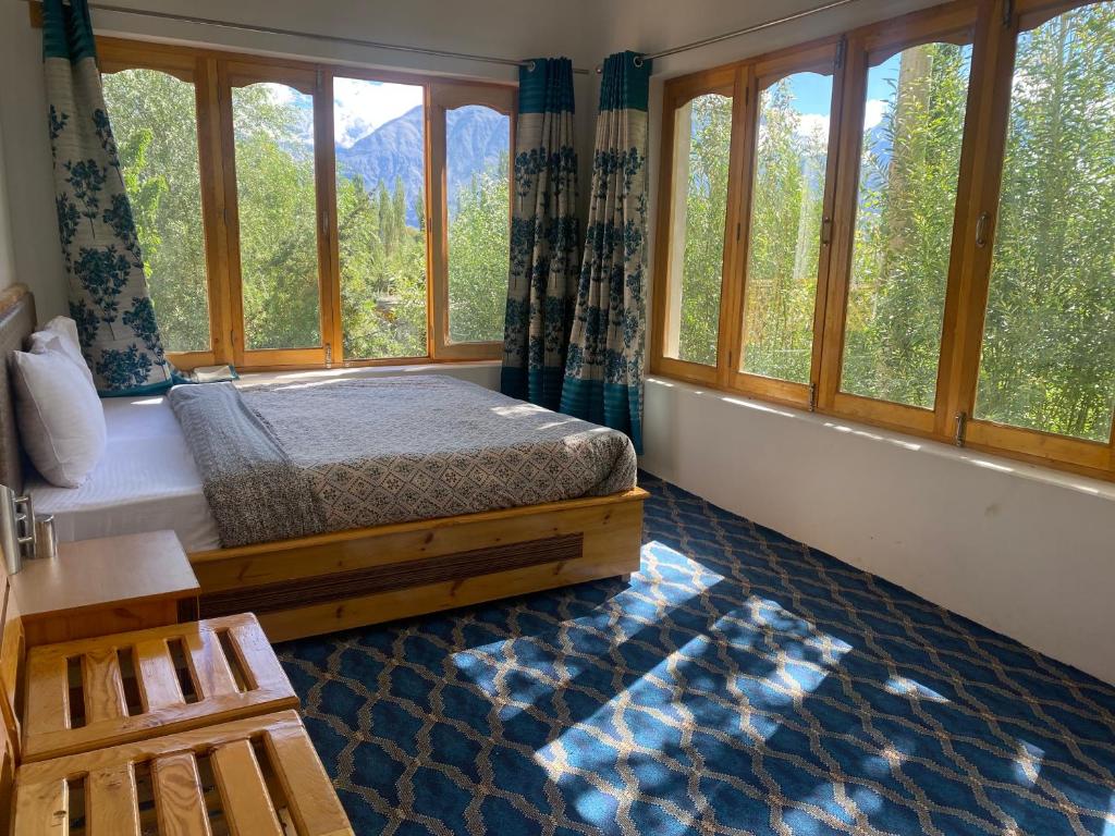 a bedroom with a bed and windows with trees at Otsal guest house nubra in Deskit