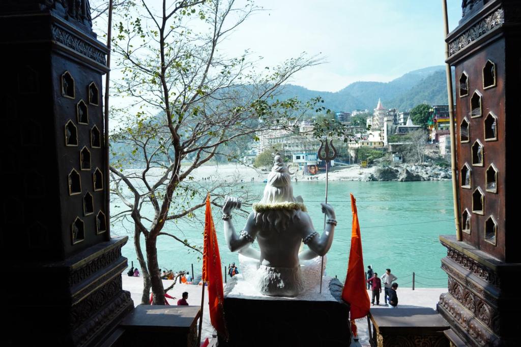 una statua seduta accanto a un corpo d'acqua di Vedic Dham Ganga a Rishikesh
