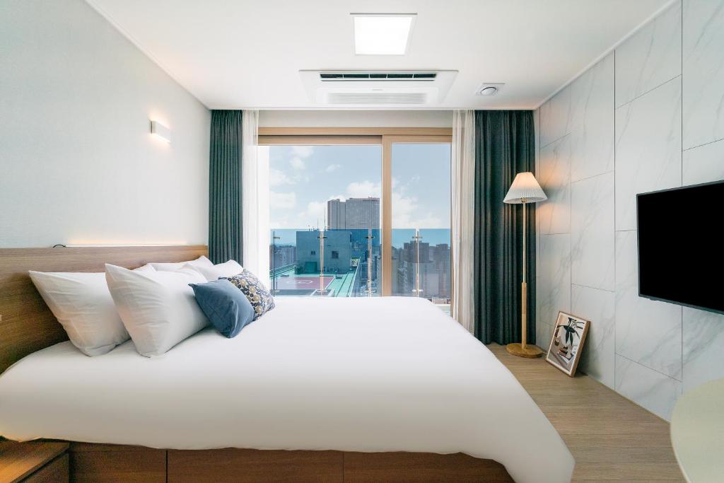 een slaapkamer met een groot wit bed en een groot raam bij Urbanstay Jeju Airport in Jeju-stad