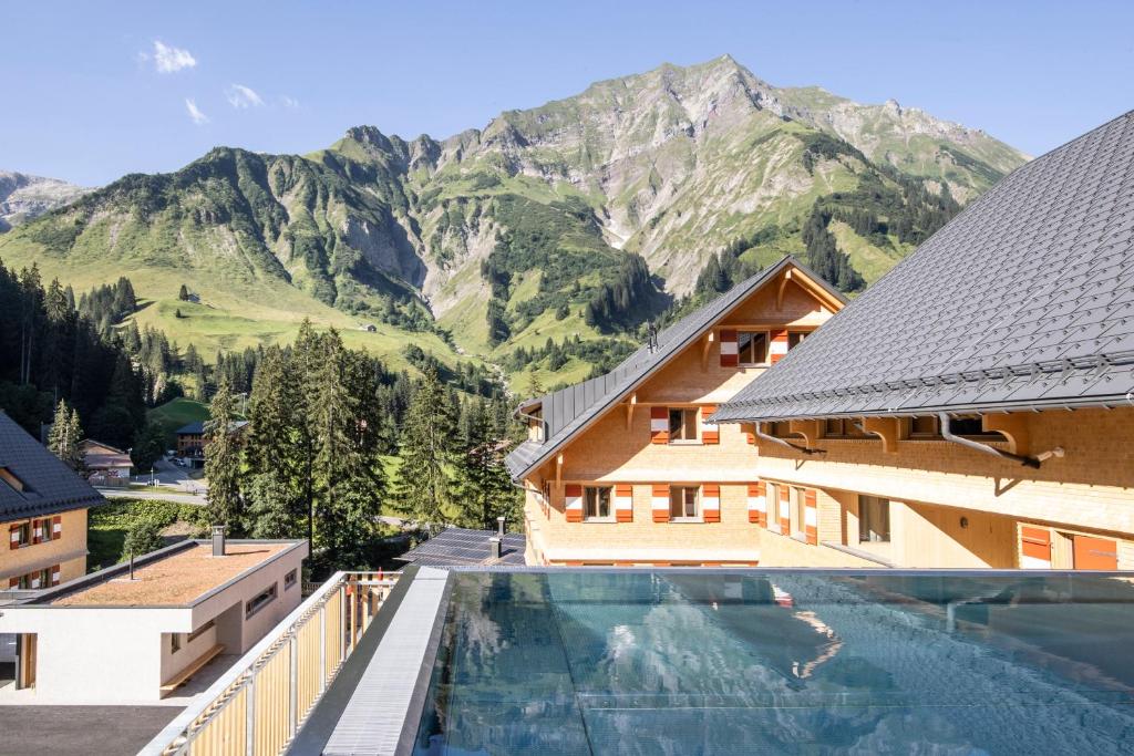 une maison avec une piscine en face d'une montagne dans l'établissement Berghaus Schröcken - Hotel Apartments Spa, à Schröcken