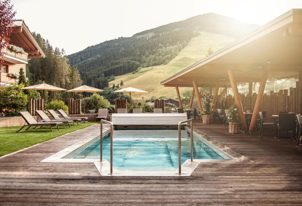 a swimming pool with a table on a wooden deck at Hotel Sonnegg in Saalbach-Hinterglemm