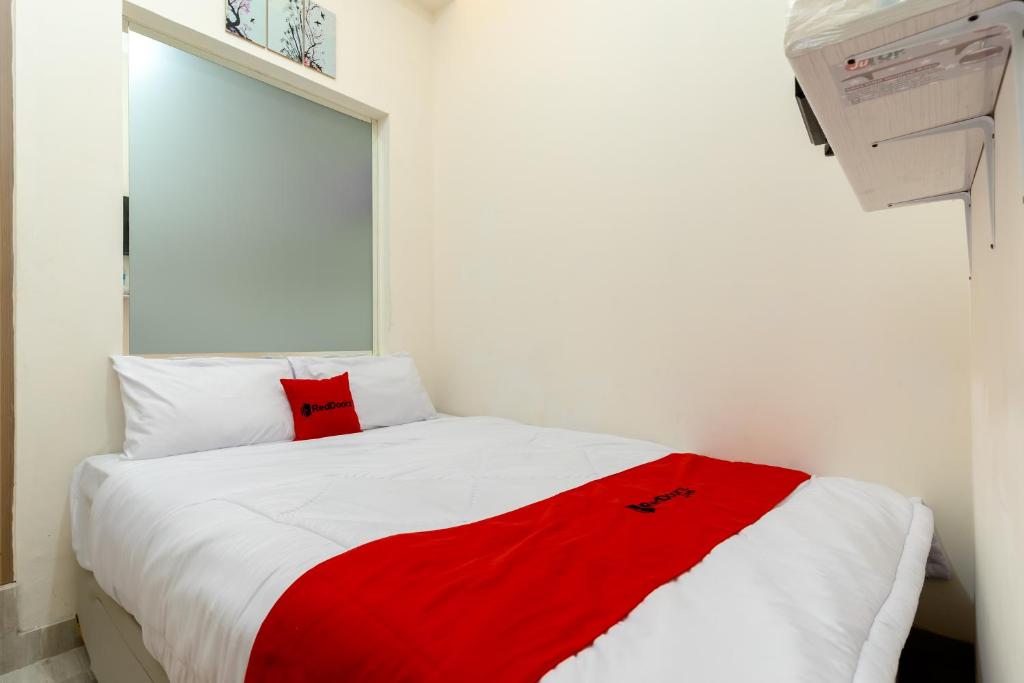 a bedroom with a red blanket on a white bed at RedDoorz Plus Near RS Royal Taruma Grogol in Jakarta