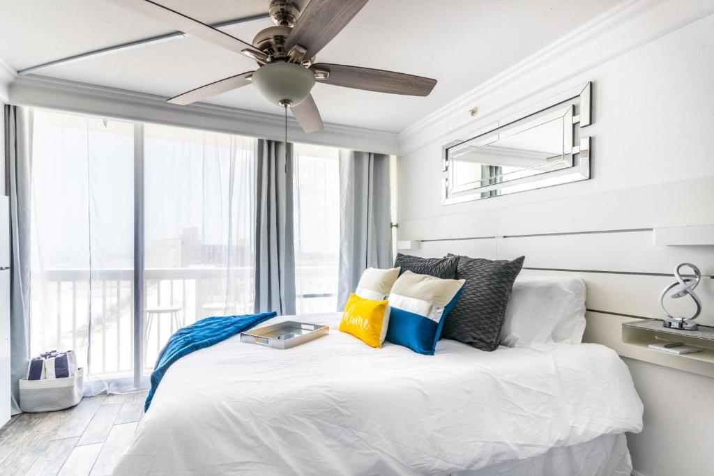 a bedroom with a white bed with a ceiling fan at Daytona Beach Resort - Ocean Front Luxury Studio in Daytona Beach