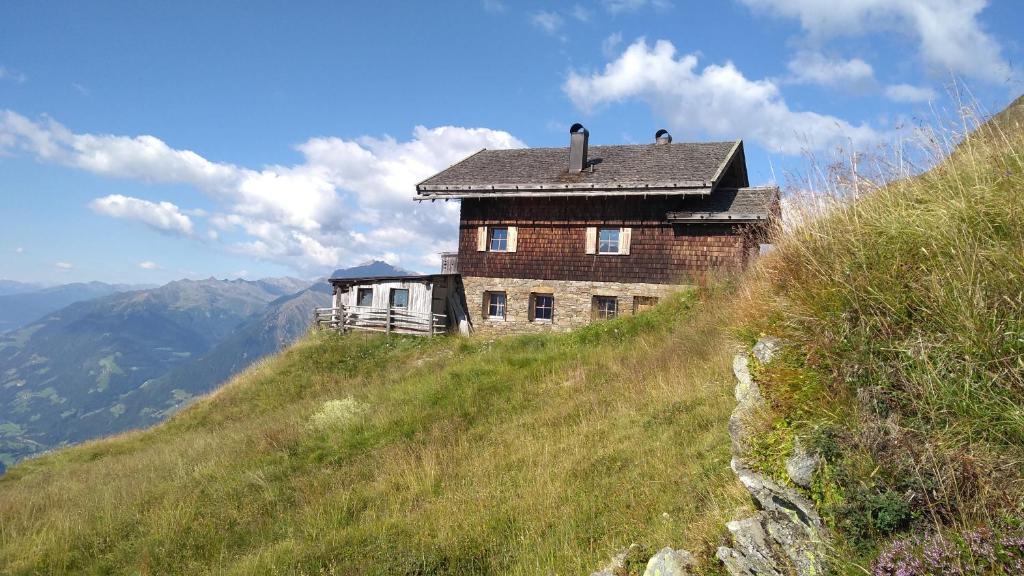 Almgasthaus Flecknerhütte في سان ليوناردو إن باسيريا: منزل على جانب تلة عشبية