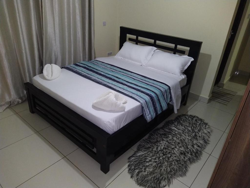 a bed with a black frame and white pillows and a rug at Amohela Serviced Apartments - Kisumu in Mamboleo