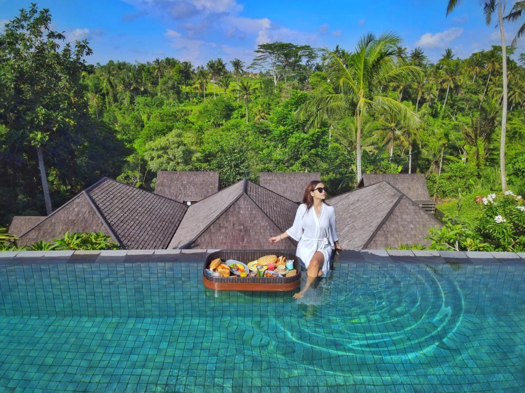a woman sitting in a swimming pool with a box of fruit at Tejaprana Bisma - CHSE Certified in Ubud
