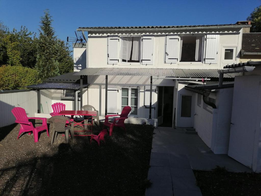 une terrasse avec des chaises roses et une table en face d'une maison dans l'établissement Maison villers sur mer 4 ou 6 PERSONNES, 2 CHAMBRES, PARKING GRATUIT, entre Deauville et Houlgate, RESERVATION UNIQUEMENT du samedi au samedi 7 nuits minimum CHEQUE de CAUTION DEMANDÉ, menage NON INCLUS, PETIT CHIEN ACCEPTÉ SAUF DANS LES CHAMBRES, à Villers-sur-Mer
