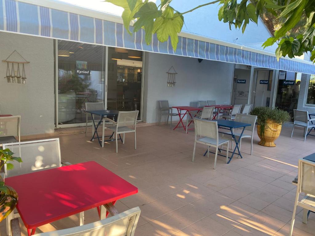 a patio with red tables and chairs and tables and chairs at Kyriad Montpellier Aéroport - Gare Sud de France in Mauguio