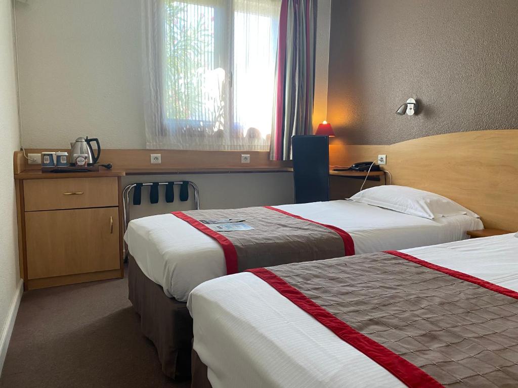 a hotel room with two beds and a window at Kyriad Montpellier Aéroport - Gare Sud de France in Mauguio