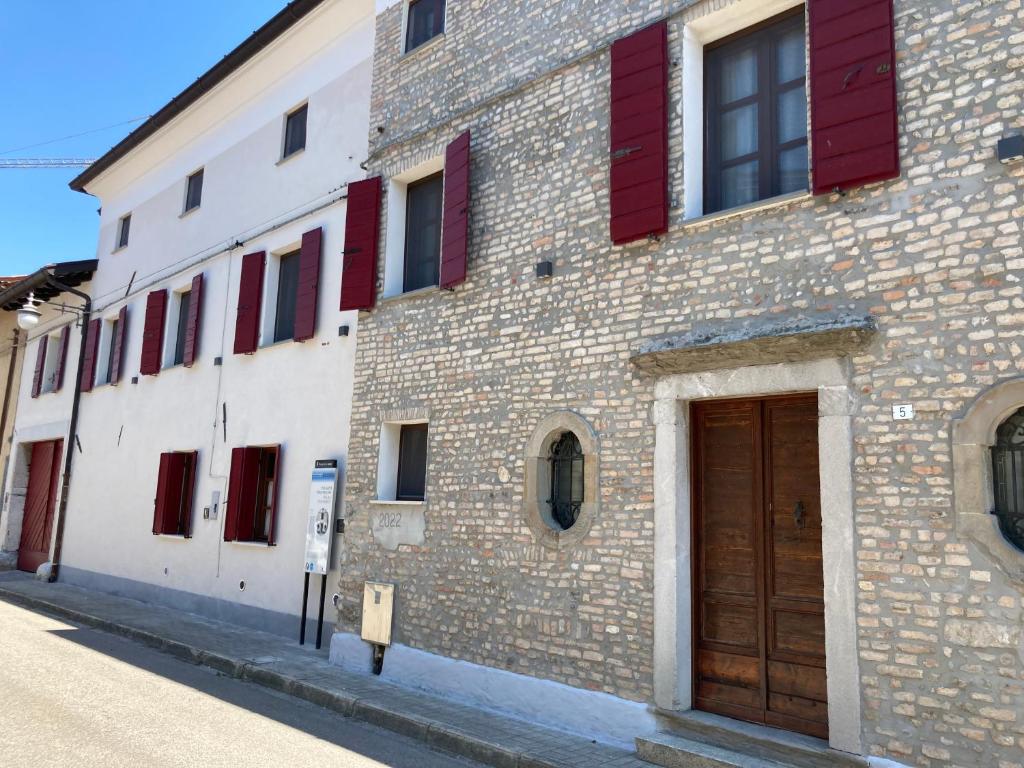 um edifício de tijolos com persianas vermelhas numa rua em Palazzo Strassoldo bed & breakfast em Teòr