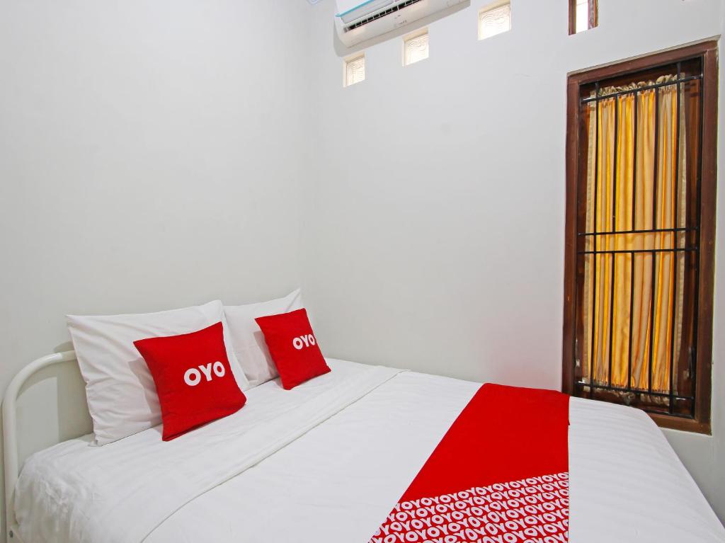 ein weißes Bett mit roten Kissen und einem Fenster in der Unterkunft OYO 91487 Ib Homestay Syariah in Tegal
