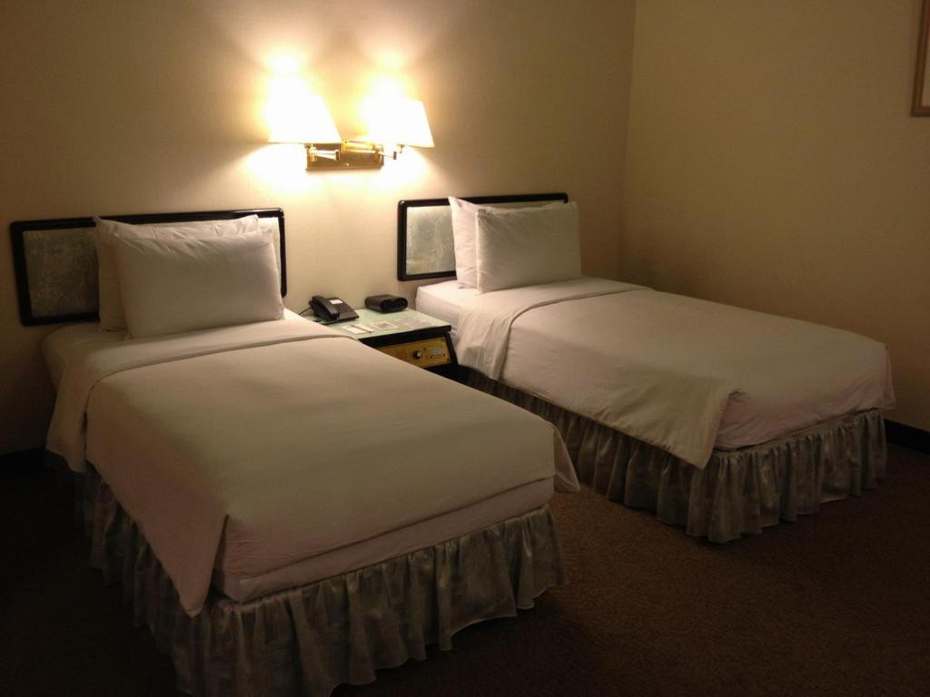 ein Hotelzimmer mit 2 Betten mit weißer Bettwäsche in der Unterkunft The Premier Hotel in Tainan