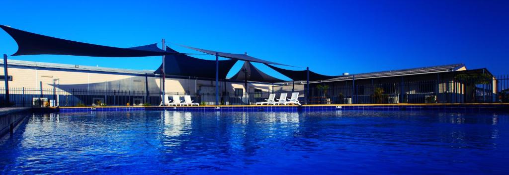 a building with a large pool of water with white chairs at Aspen Karratha Village in Karratha