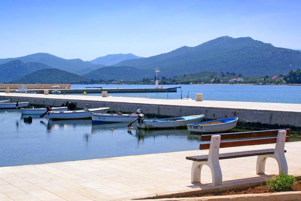 a bench sitting next to a body of water with boats at Family Room Drace 4550a in Drače