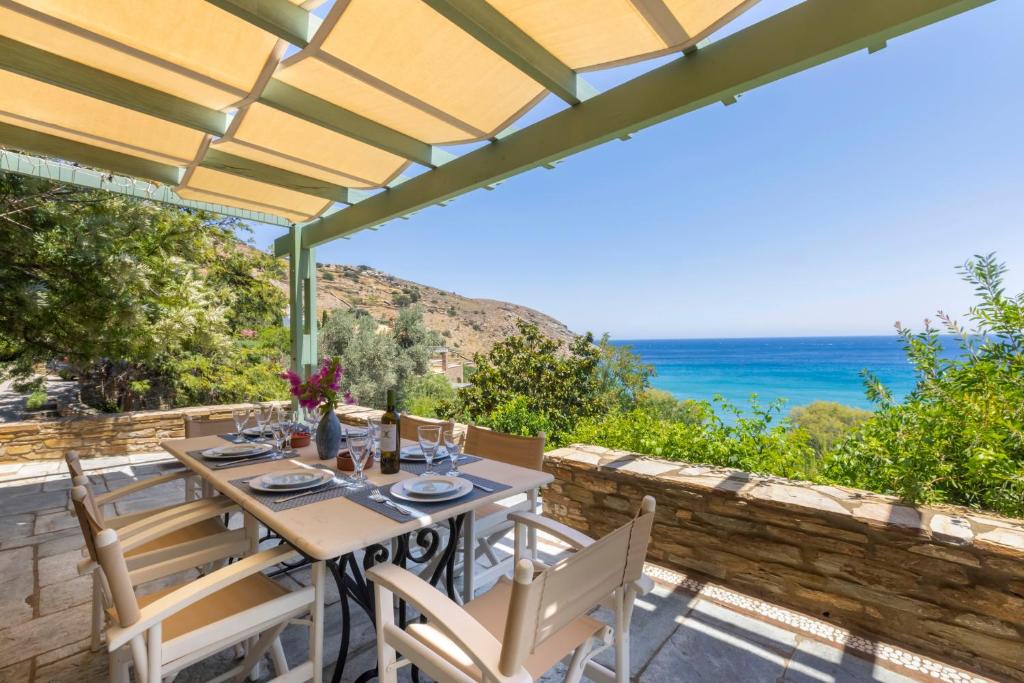 a table and chairs on a patio with a view of the ocean at Sun-rock house by the sea in Andros