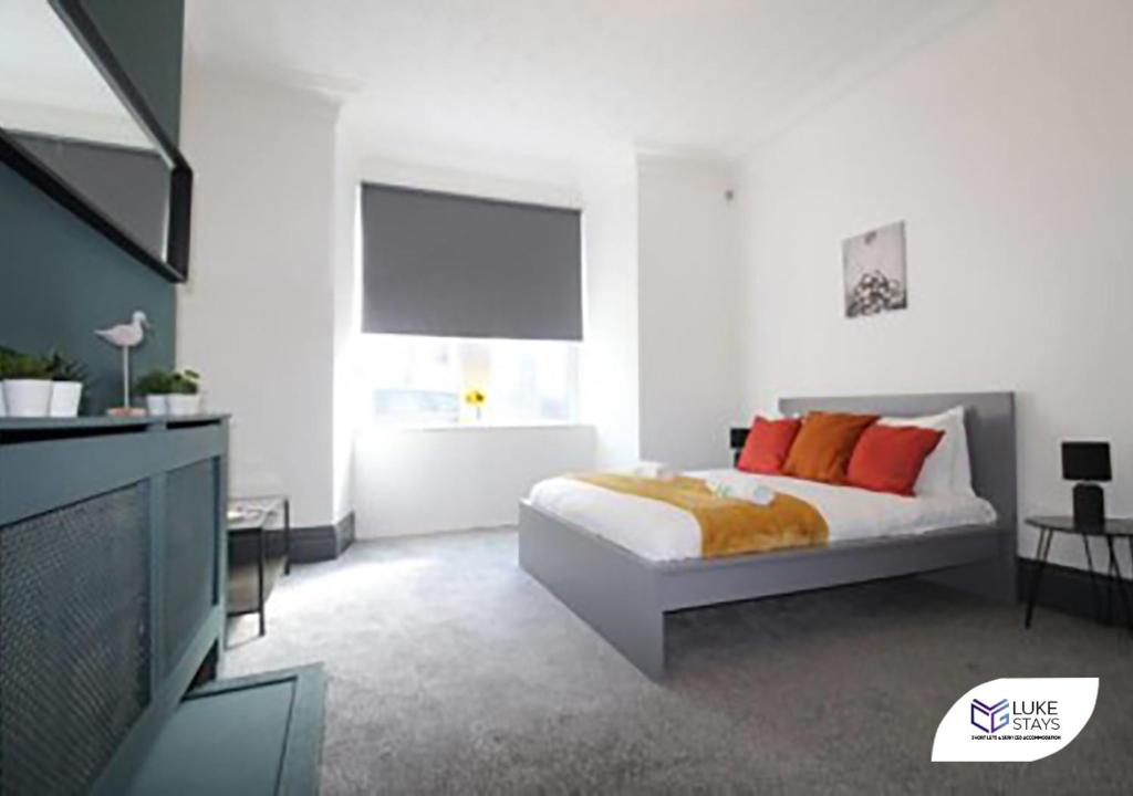 a white bedroom with a bed with orange pillows at Luke Stays - Brinkburn Avenue in Gateshead