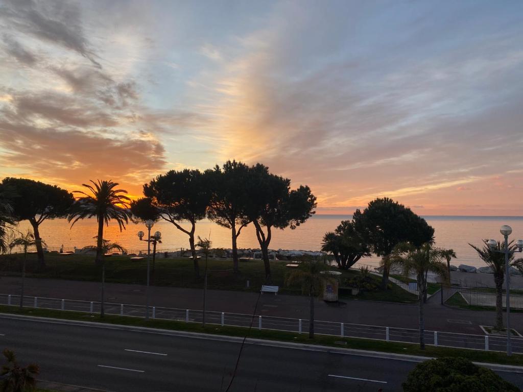 un coucher de soleil sur une route avec des palmiers et l'océan dans l'établissement Appartement Nice Promenade, à Nice