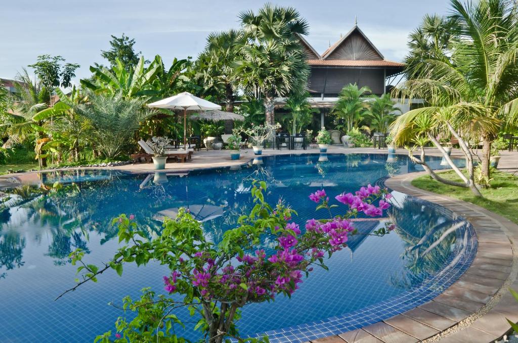 a swimming pool in front of a resort with purple flowers at Battambang Resort in Battambang